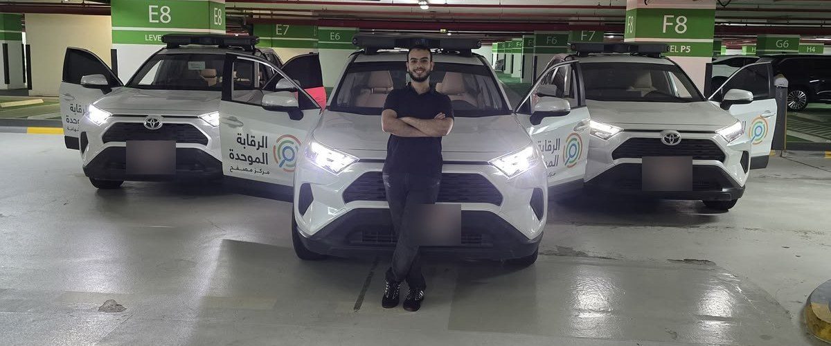 Ali Ahmed Samir standing with arms crossed in front of three white SUVs with open doors in an Abu Dhabi car park; licence plates are blurred